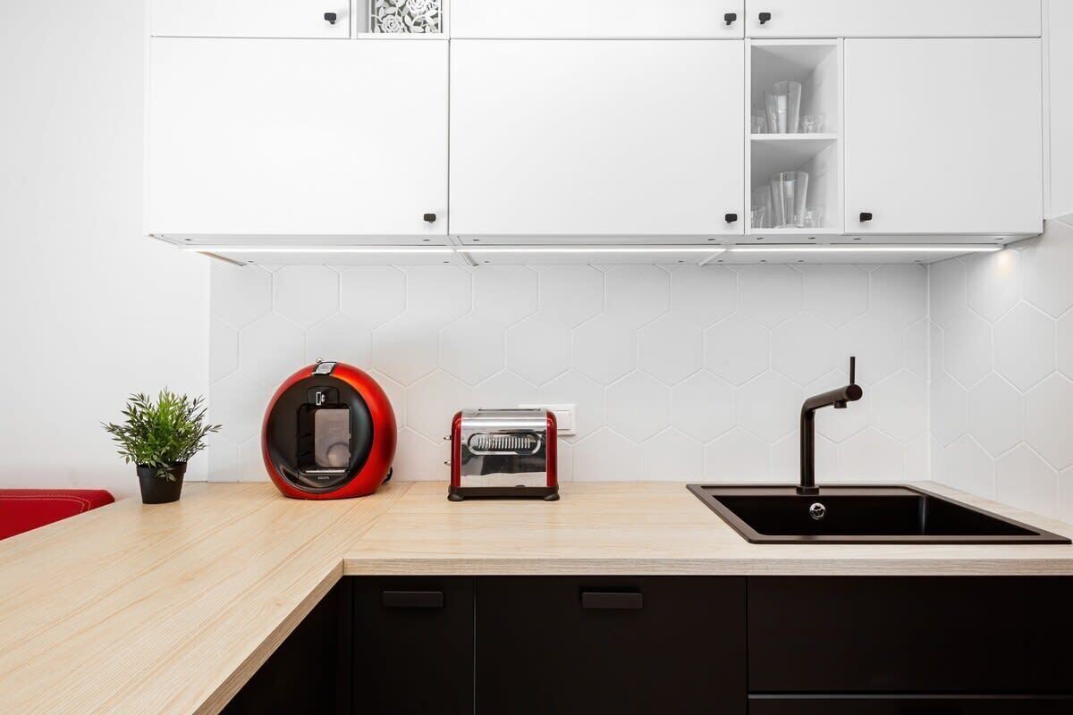 Une cuisine moderne avec des meubles blancs, un évier noir, un appareil électroménager rouge et un grille-pain.