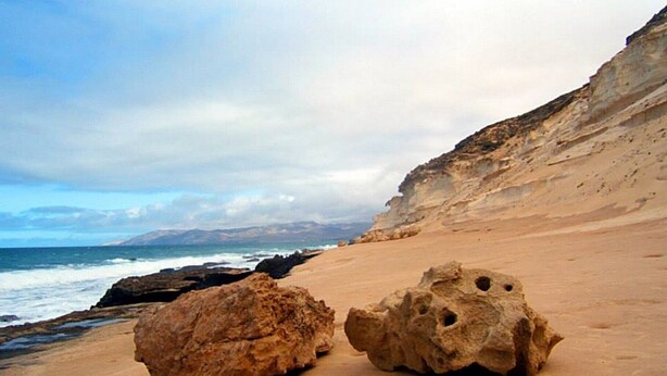 A sandy beach with two large rocks and a cliff in the background. - Casa Sony El Cotillo (El Cotillo)