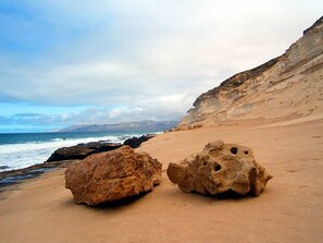 A sandy beach with two large rocks and a cliff in the background. - Casa Sony El Cotillo (El Cotillo)