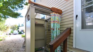 A residential entryway with a wooden staircase, a door with a window, and a covered outdoor area with a shower.