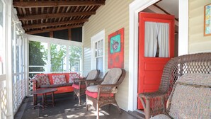 A covered porch with wicker furniture, a red door, and a painting of a fish.