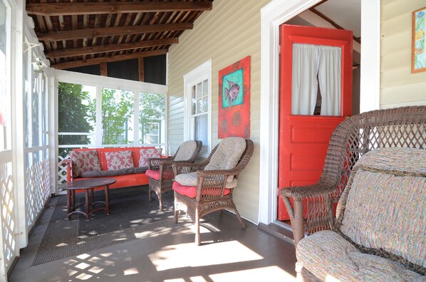 A covered porch with wicker furniture, a red door, and a painting of a fish. - 4 BR Beach Home in 2nd Ocean Block, 101 Hickman Street, South Rehoboth Beach (Rehoboth Beach)