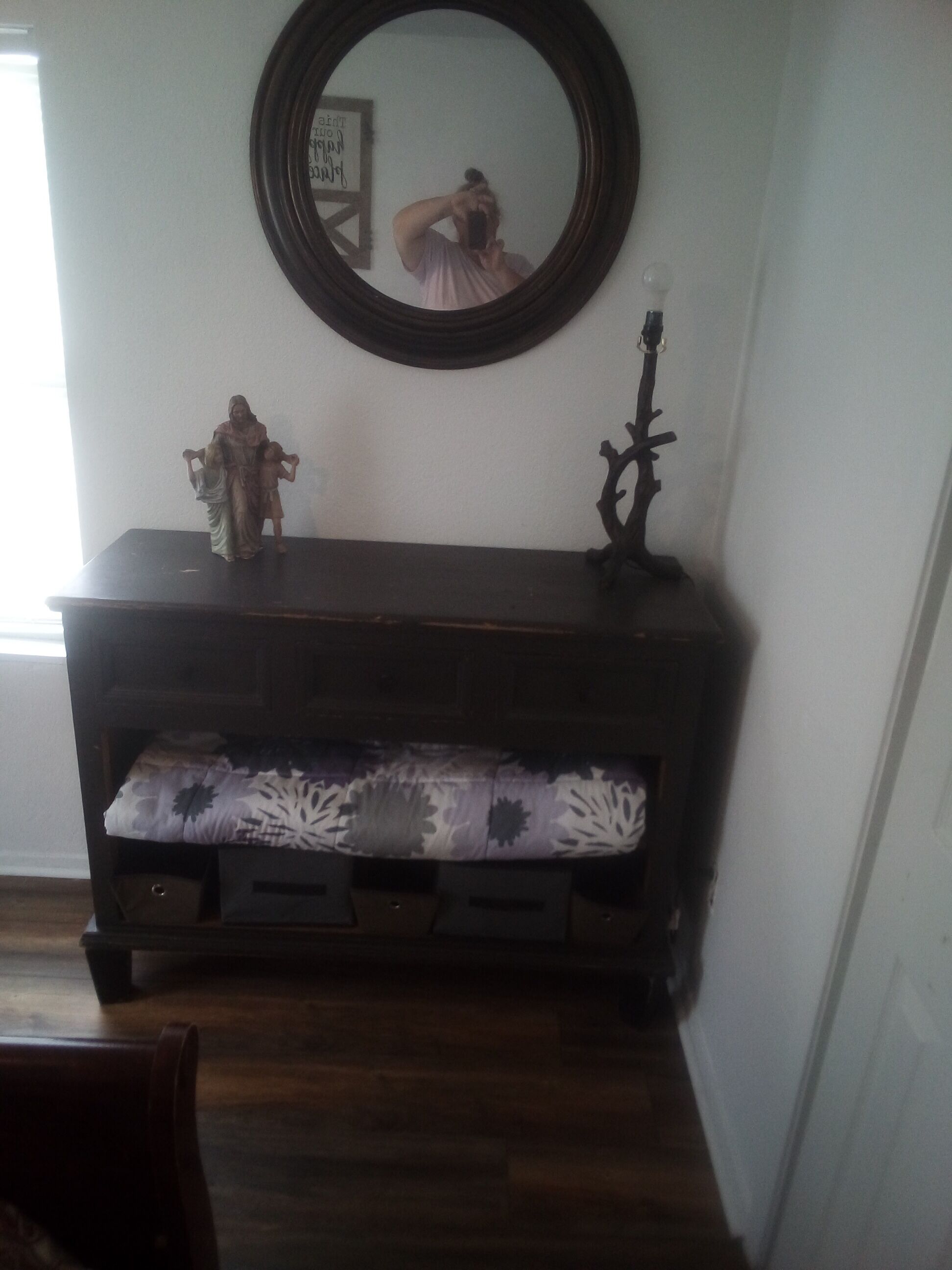 A dark wooden console table with a floral cushion, a small statue, and a candelabra.