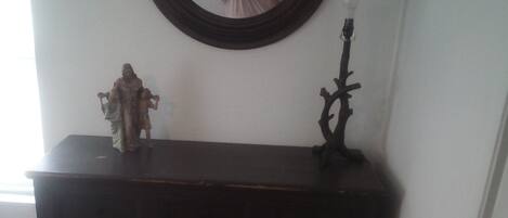 A dark wooden console table with a floral cushion, a small statue, and a candelabra.