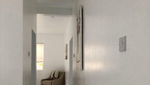 Un corridoio con un divano beige, pareti bianche e pavimento piastrellato.