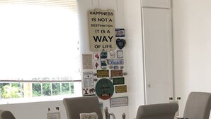 Zona pranzo con tavolo in legno e quattro sedie grigie. Diverse decorazioni alle pareti, tra cui un cartello con la scritta: "Happiness is not a destination, it is a way of life".