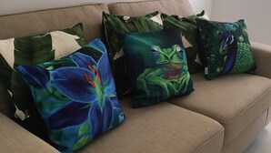 Un divano beige con tre cuscini decorativi con motivi floreali e disegni di pavone.