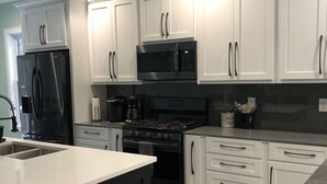 A modern kitchen with white cabinets, a black refrigerator, a stainless steel microwave, and a gas stove. - Located at Silver Lake with access to Silver Lake and sand dunes. (Mears)