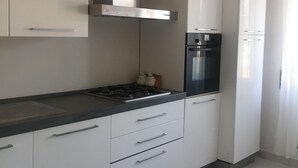 A modern kitchen with white cabinets, a stainless steel range hood, a built-in oven, and a refrigerator.