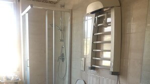 A bathroom with a glass-enclosed shower, two toilets, a sink, and a towel rack.