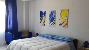 A bedroom with a large bed, a blue chair, and three abstract paintings on the wall.