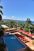 Una piscina con sillas de descanso y sombrillas, rodeada de palmeras y vista al océano.