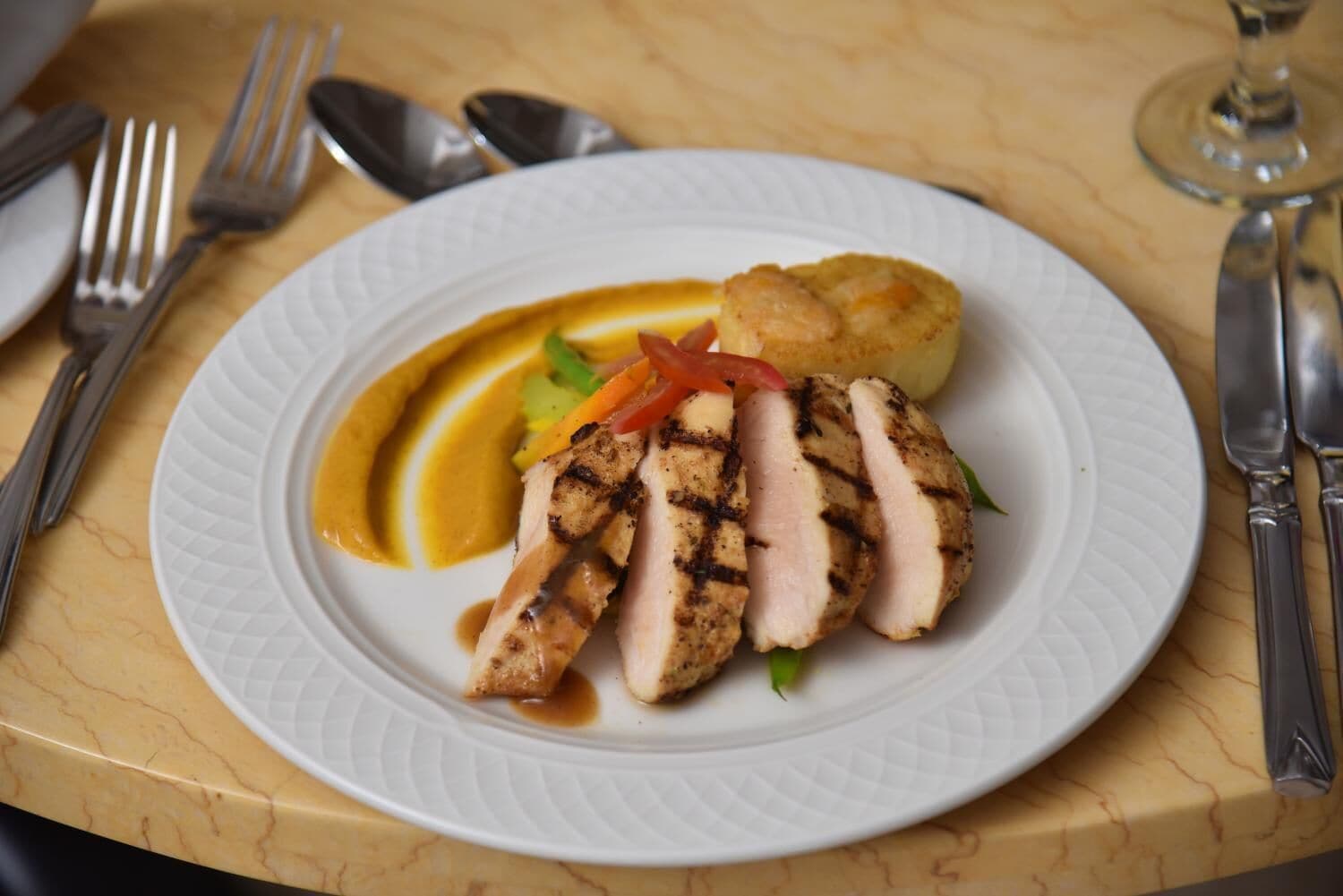 Une assiette contenant de la viande grillée, des légumes et un accompagnement, posée sur une table en marbre.