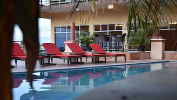 Uma área de piscina com cadeiras de sol vermelhas e plantas em vasos.