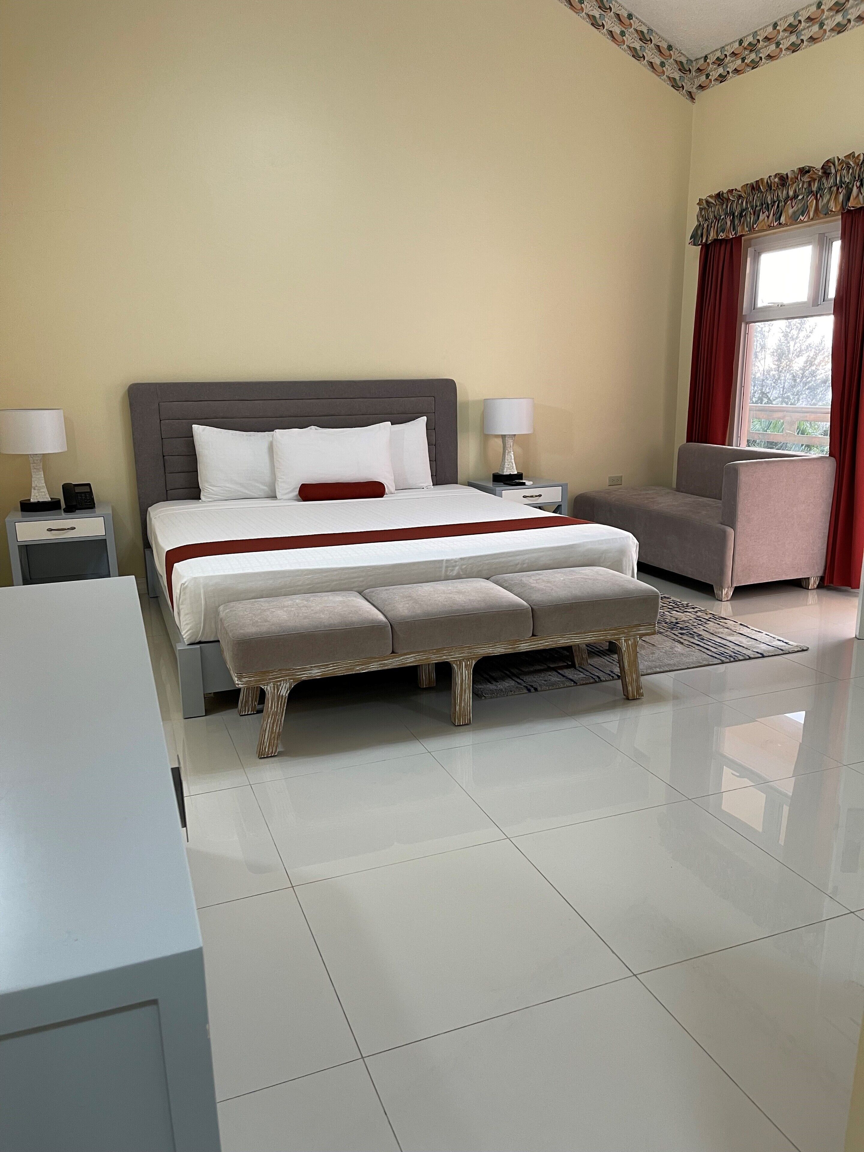 A neatly arranged bedroom with a large bed, bedside tables with lamps, a bench, and a sofa.