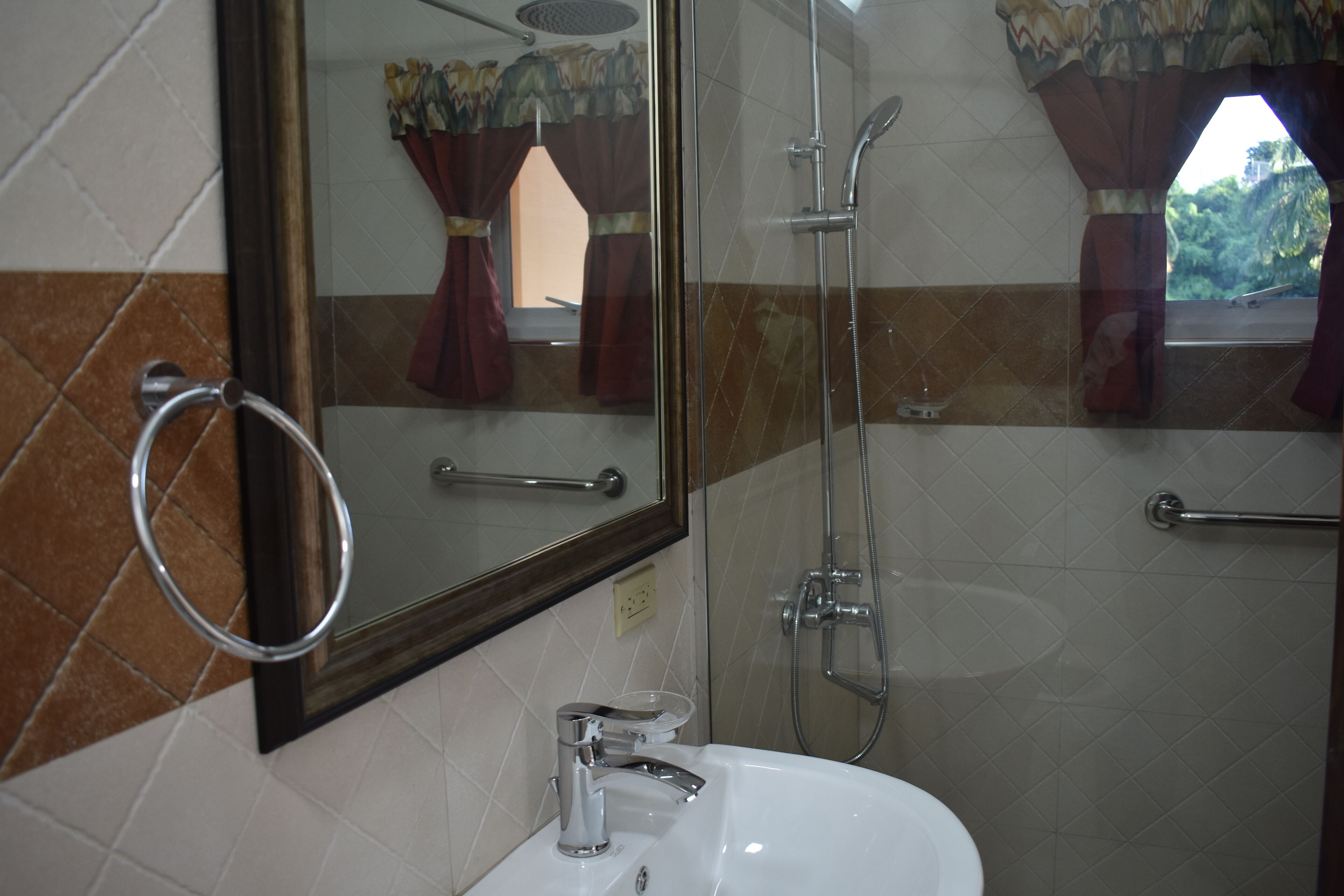 Un baño con ducha de vidrio, lavamanos blanco y espejo con argolla para toalla.