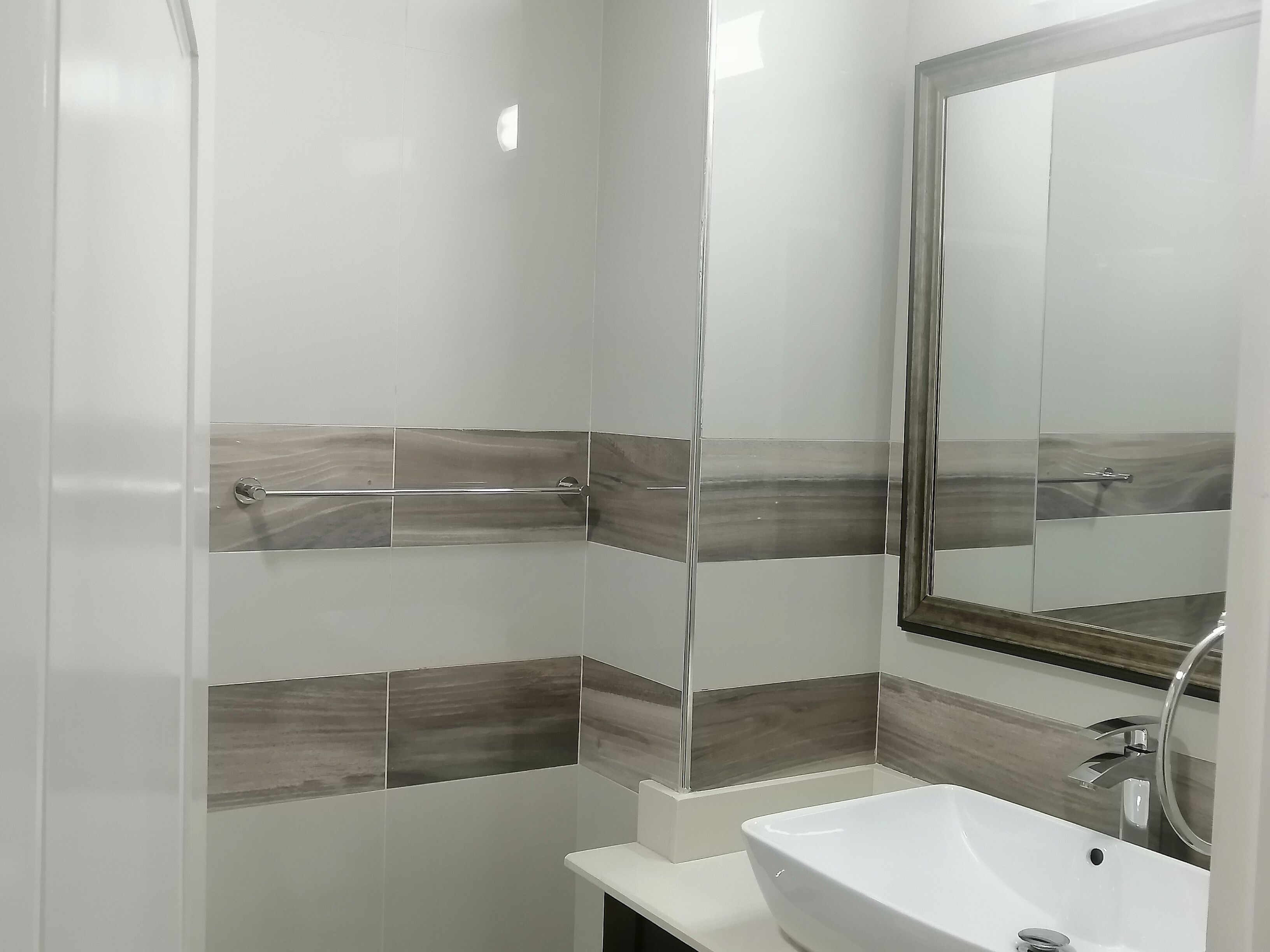 A bathroom with a white sink, a mirror, and tiled walls with a wood-like pattern.