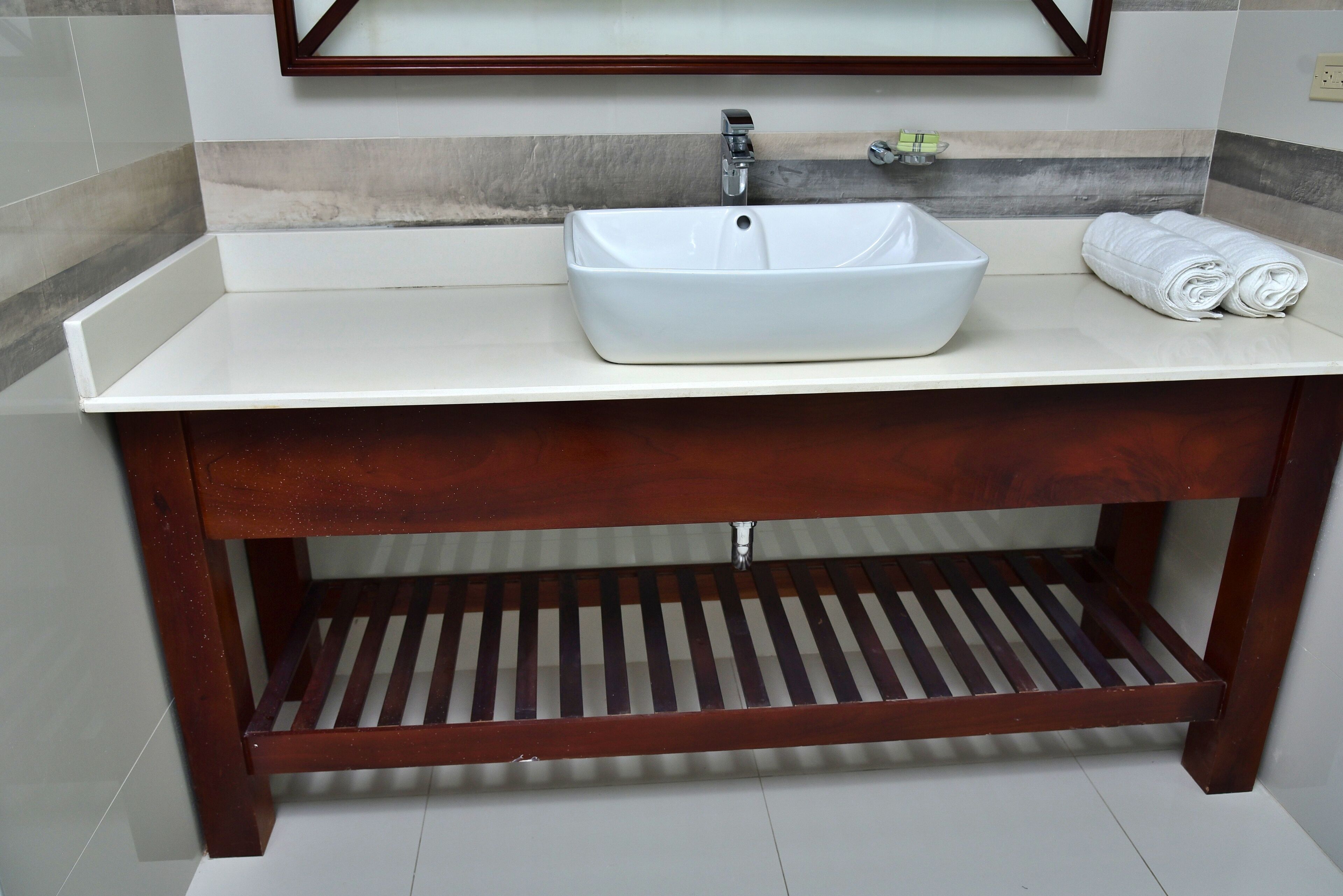 A bathroom with a white sink, wooden vanity, and a towel rack.