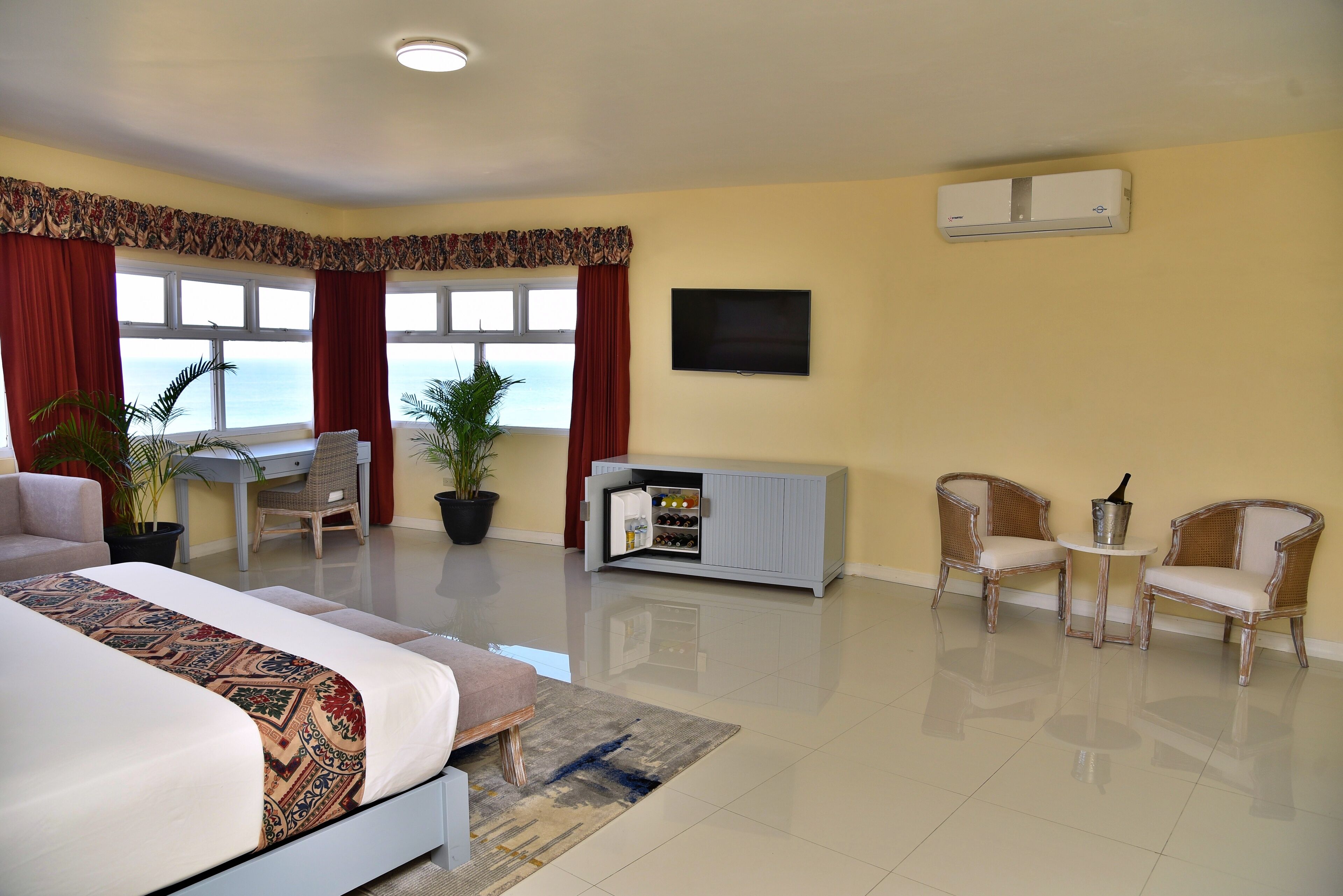 A hotel room with a bed, desk, two chairs, a TV, and a minibar.