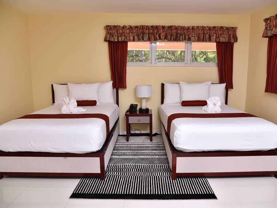 A double room with two beds, a nightstand, a lamp, and a window with curtains.