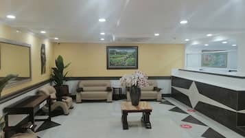 A reception area with a reception desk, two armchairs, a sofa, a potted plant, and a painting on the wall.