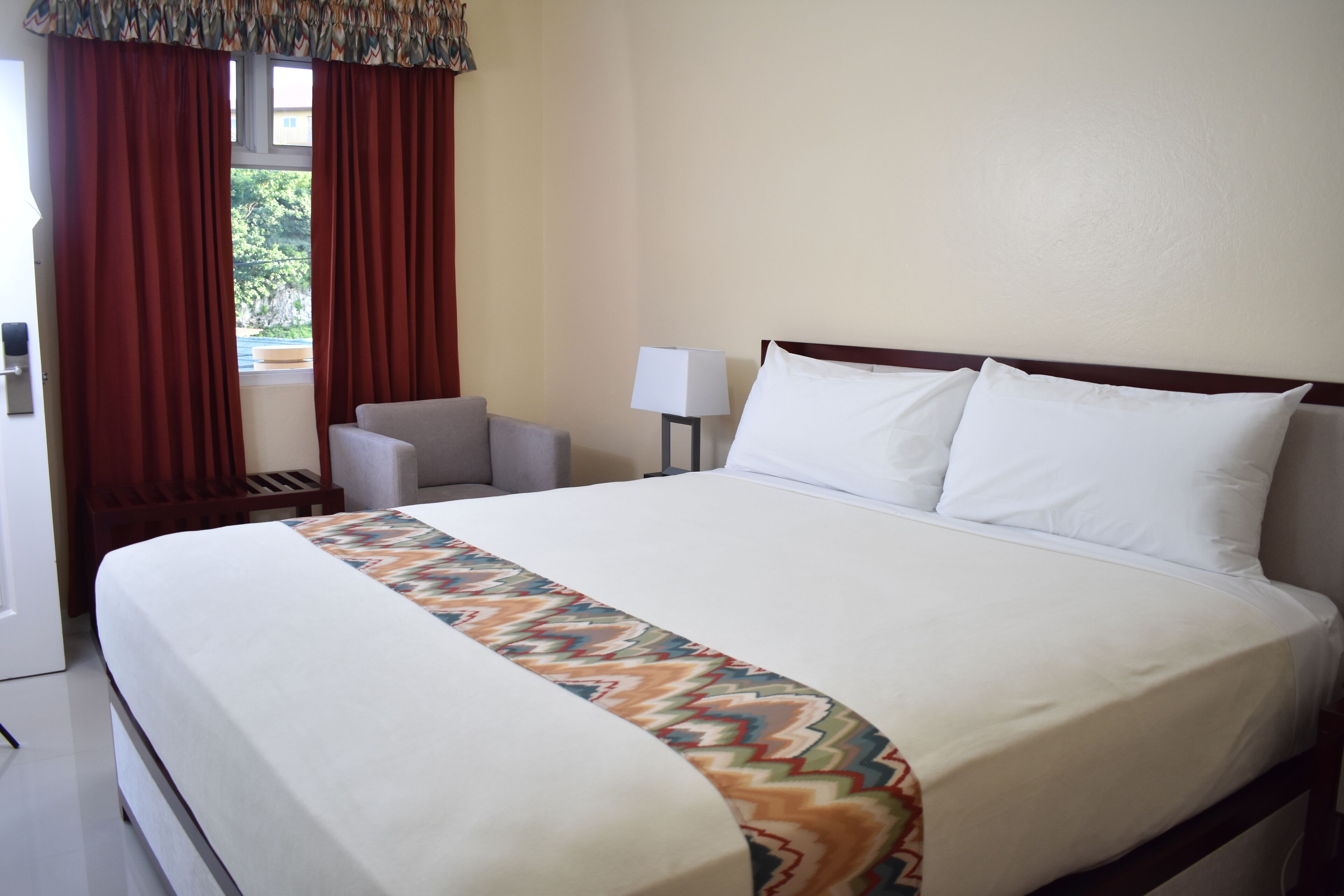 A hotel room with a large bed, a bedside table with a lamp, a chair, and a window with curtains.