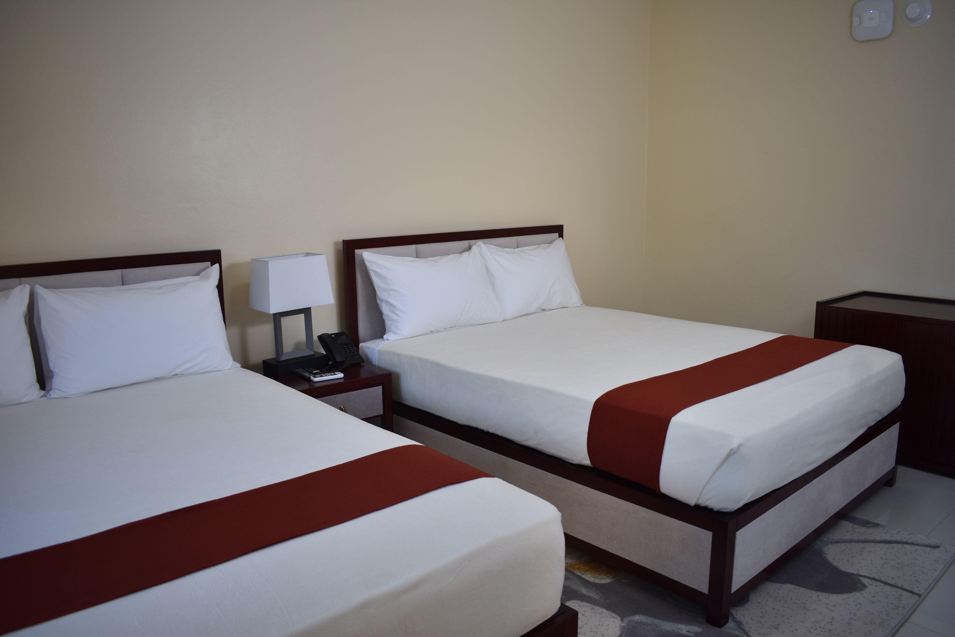 Two single beds with wooden frames, white bedding, and red bedspreads. Each bed has a bedside table with a lamp and a phone.