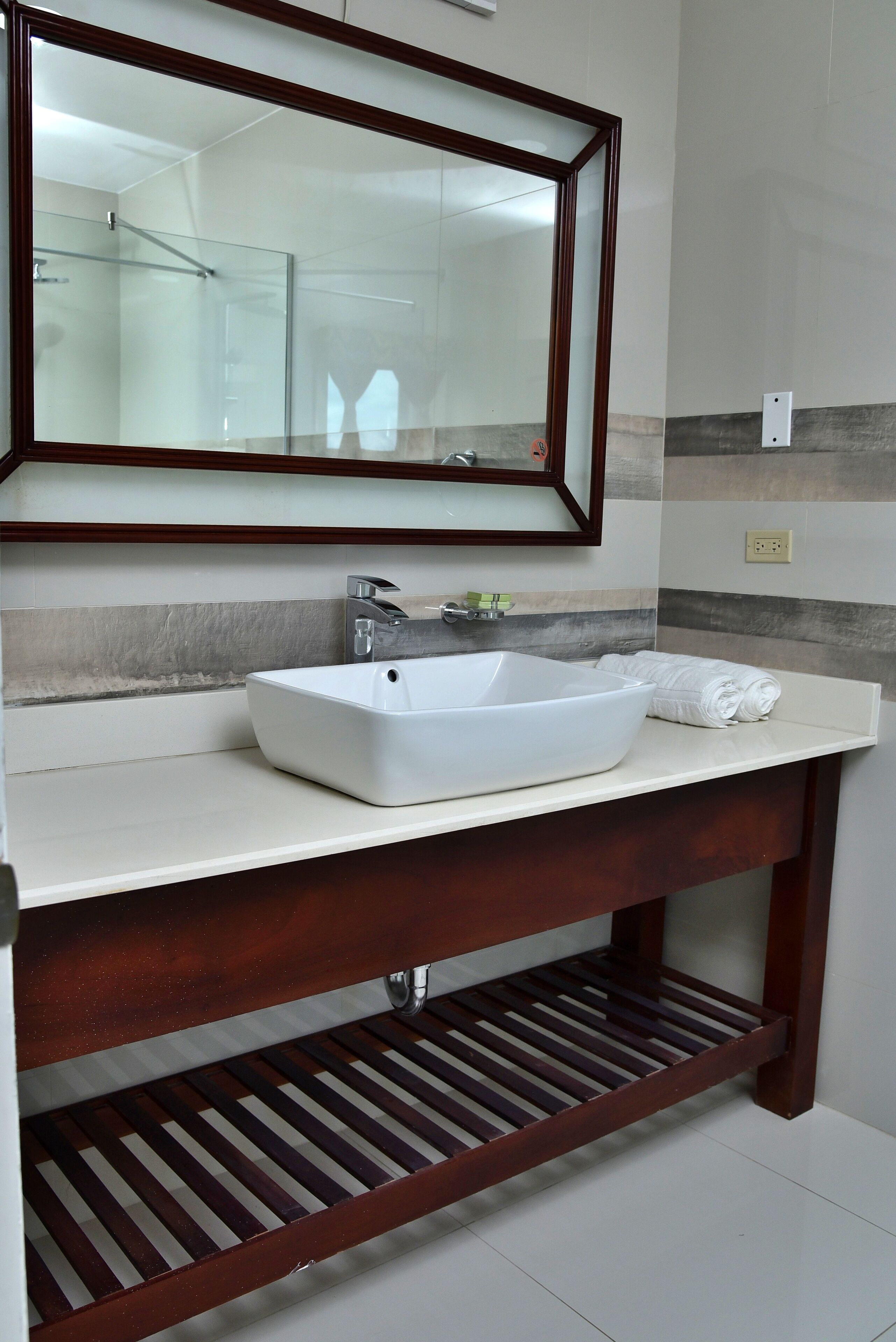 Un baño con lavamanos blanco, espejo y toallero.