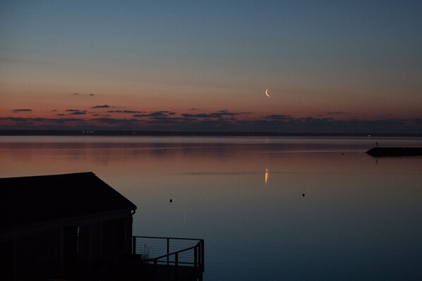 A calm body of water with a crescent moon in the sky, a dock, and a building with a railing. - Beachfront, East End, 2 BR, 2BA, Private Deck, Parking, Dog Friendly (Provincetown)