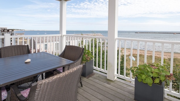 A covered outdoor area with a table and chairs, a view of the sea, and potted plants. - Beachfront, East End, 2 BR, 2BA, Private Deck, Parking, Dog Friendly (Provincetown)