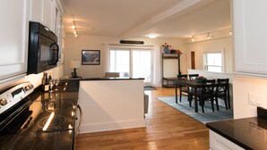 A modern kitchen with a black stove, white cabinets, and a dining area with a table and chairs. - Beachfront, East End, 2 BR, 2BA, Private Deck, Parking, Dog Friendly (Provincetown)
