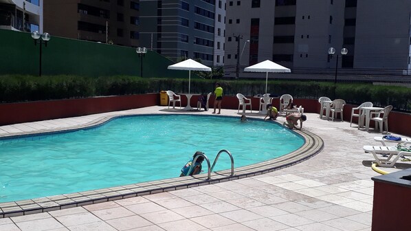 Una piscina con plataforma de azulejos, rodeada de sillones de descanso y sombrillas.