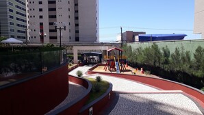 Une aire de jeux avec un toboggan et des structures d’escalade, entourée d’une zone pavée bordée de rouge et agrémentée de petites plantes.