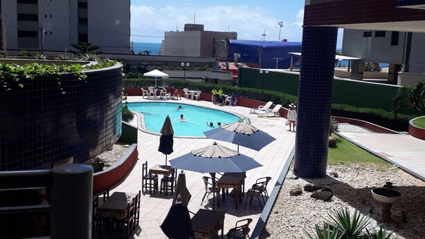 Un espace piscine aménagé sur le toit, avec des chaises longues et des parasols, entouré d’immeubles et offrant une vue sur l’océan.