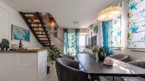 A modern kitchen with a wooden staircase, a dining area with a table and chairs, and a large window with blue floral curtains. - Cozy apartment in Zadar with WiFi (Zadar)