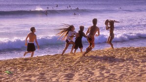 A sandy beach with people running and playing in the water.