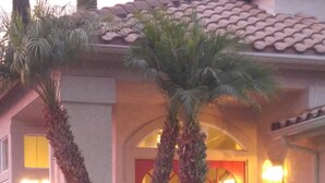 A house with a red door, two palm trees, and a well-maintained lawn.