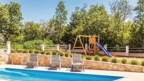 Una piscina con lettini e un’area giochi in legno con scivolo.