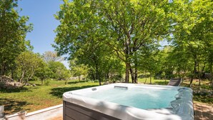 Una vasca idromassaggio in un giardino con alberi e un pontile di legno.