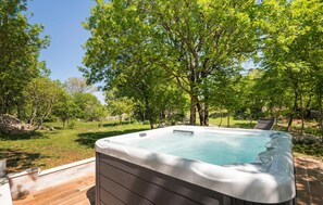 Relax in a serene outdoor setting with a hot tub surrounded by lush greenery.