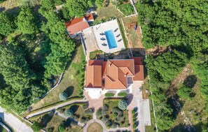 Surrounded by lush greenery, this property features a main building with a red-tiled roof and a swimming pool area.