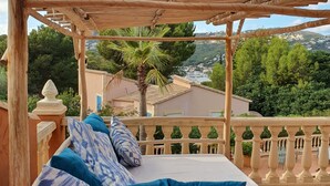Eine hölzerne Pergola mit einem Bett und Kissen, mit Blick auf eine malerische Landschaft mit Bäumen und Gebäuden.