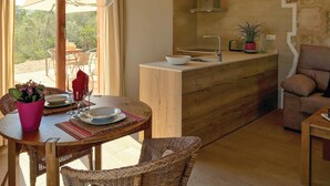 A modern kitchen with a wooden countertop, a sink, and a potted plant. There is a dining area with wicker chairs and a table set for two. - Lovely home in Son Carrió with WiFi (Son Carrió)