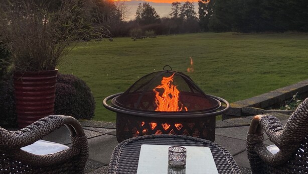A patio with a fire pit, wicker chairs, and a view of the sunset over a grassy area.