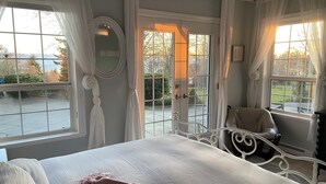 A bedroom with a large bed, a chair, and a view of the outdoors through a glass door.