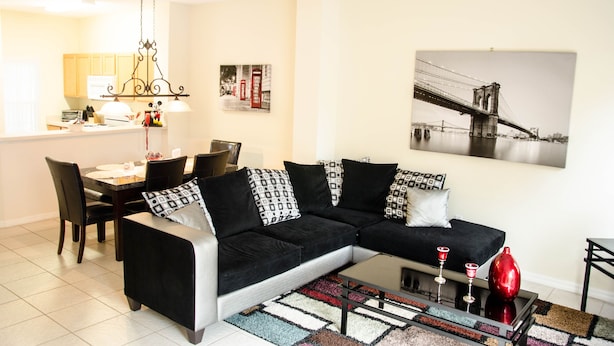 A living room with a black and white sectional sofa, a dining area with a table and chairs, and a kitchen in the background. - Lake View 3 Bedroom Villa. Enjoy Private Hot Tub! (Kissimmee)