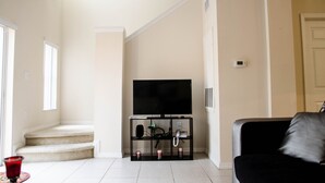 A living room with a flat-screen TV on a black stand, a staircase leading to another level, and a door on the right. - Lake View 3 Bedroom Villa. Enjoy Private Hot Tub! (Kissimmee)