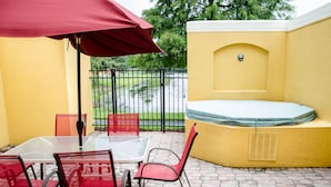 An outdoor patio with a glass table and red chairs, a red umbrella, and a yellow wall with a hot tub. - Lake View 3 Bedroom Villa. Enjoy Private Hot Tub! (Kissimmee)