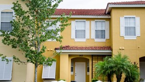 A yellow building with white shutters, a number 142, and a small porch with a door. - Lake View 3 Bedroom Villa. Enjoy Private Hot Tub! (Kissimmee)