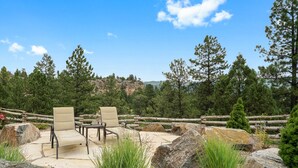 An outdoor seating area with chairs and a table, surrounded by rocks and plants, with a view of trees and a distant mountain range. - Large newly updated condo in close proximity to town and summer adventures!  (Durango)